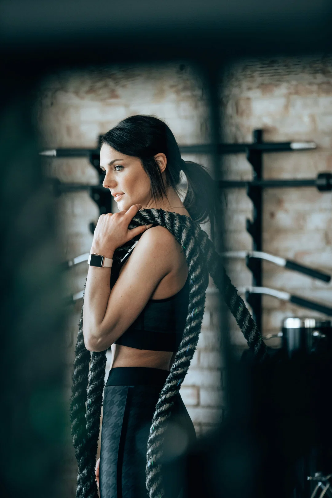 Frau in Sportbekleidung hält Battle Ropes in einem Fitnessstudio und schaut nachdenklich zur Seite.